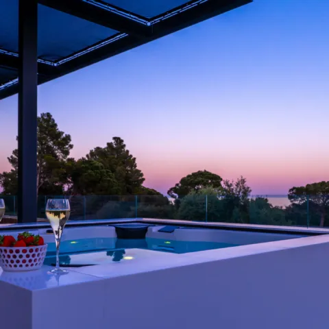 Un jacuzzi de l'Hôtel Villa Padulaccia au crépuscule sous une pergola, deux coupes et une coupelle de fraises sur le rebord, la mer au loin