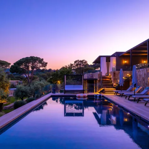 La piscine chauffée de l'Hôtel Villa Padulaccia au crépuscule, bordée de transats et de terrasses éclairées