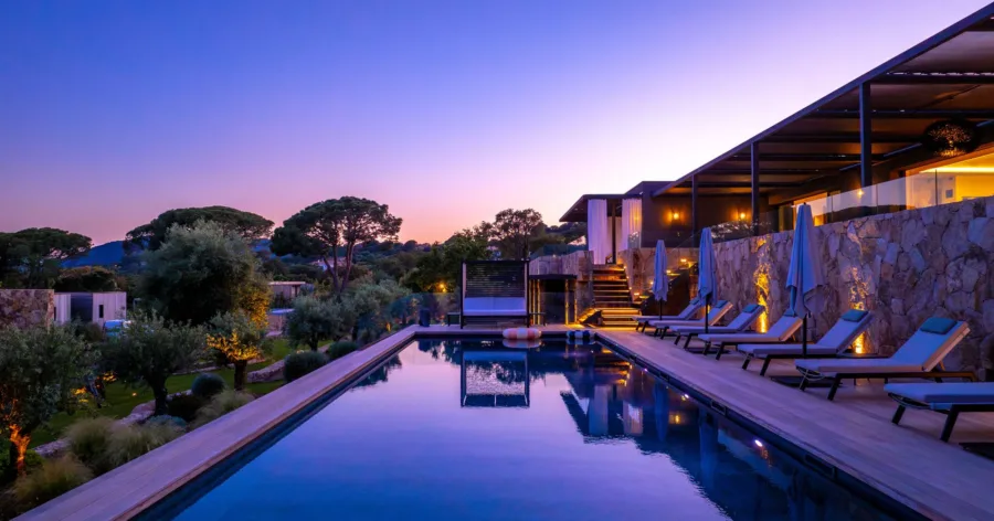 La piscine chauffée de l'Hôtel Villa Padulaccia au crépuscule, bordée de transats et de terrasses éclairées