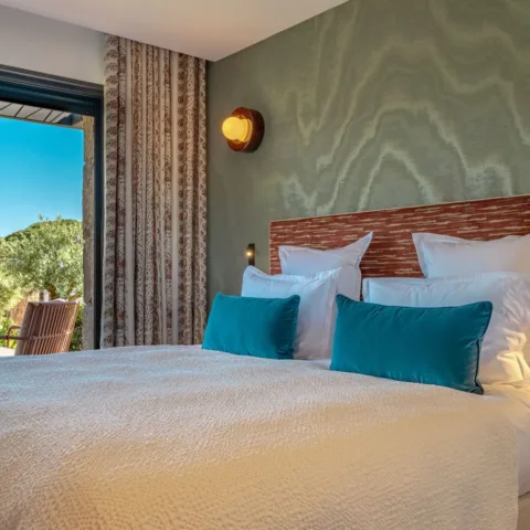 Une chambre de l'Hôtel Villa Padulaccia : grand lit, coussins bleu canard et baie vitrée ouverte sur le jardin