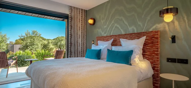 Une chambre de l'Hôtel Villa Padulaccia : grand lit, coussins bleu canard et baie vitrée ouverte sur le jardin