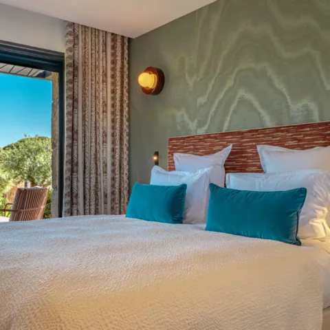 Une chambre de l'Hôtel Villa Padulaccia : grand lit, coussins bleu canard et baie vitrée ouverte sur le jardin
