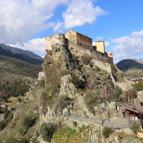 La citadelle de Corte sur son éperon rocheux, vue depuis le belvédère, vallées et montagnes autour.