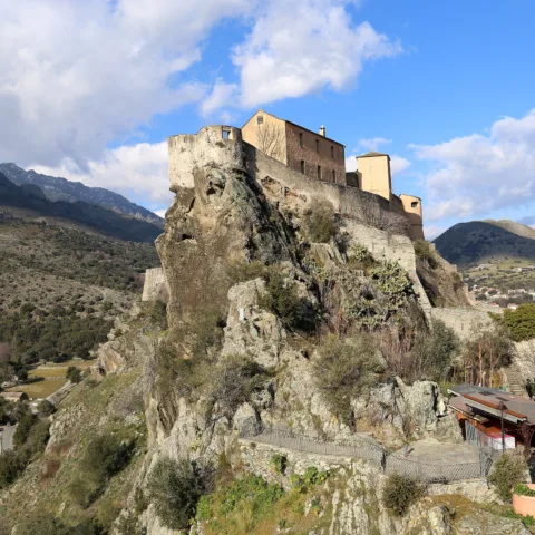 La citadelle de Corte sur son éperon rocheux, vue depuis le belvédère, vallées et montagnes autour.