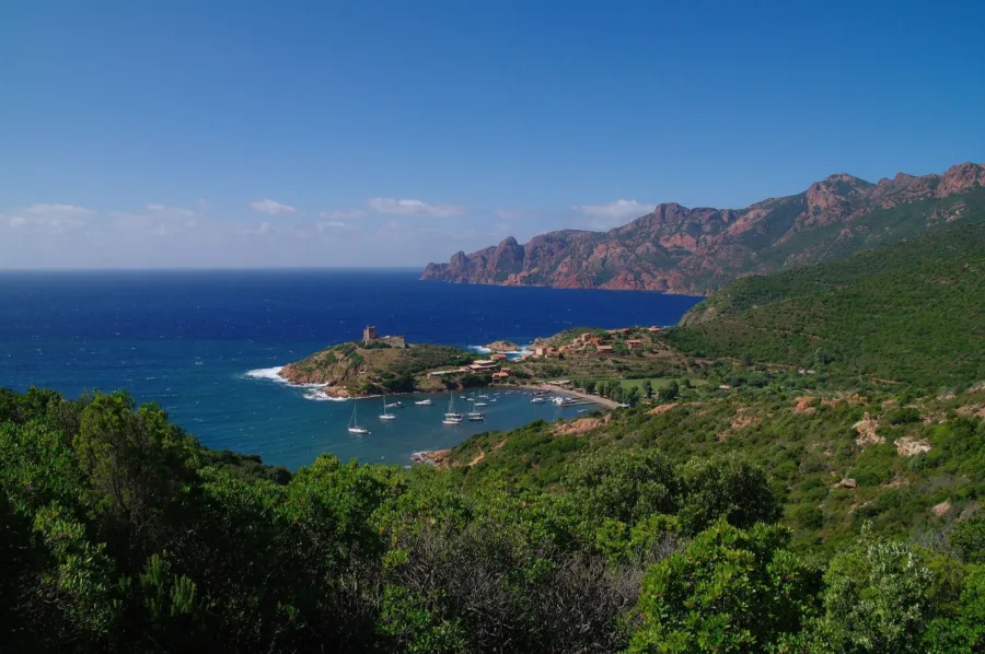La baie de Girolata et son fortin génois, voiliers au mouillage, falaises rouges du golfe en arrière-plan.