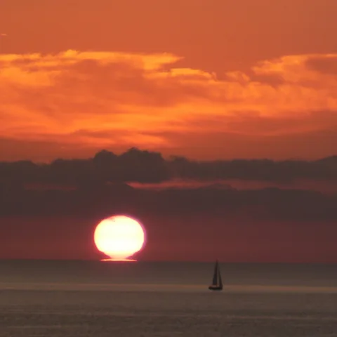 Lever du soleil sur la mer au large de Pinarello, un voilier à l'horizon (juillet 2008).