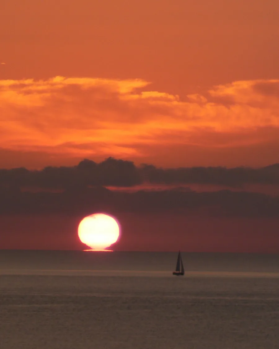Lever du soleil sur la mer au large de Pinarello, un voilier à l'horizon (juillet 2008).