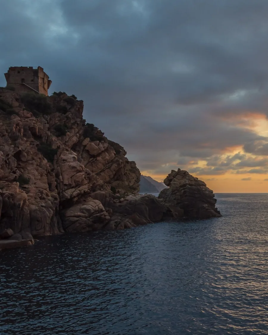 La tour génoise de Porto sur son rocher de granit, au soir, sous des nuages sombres, au-dessus du golfe de Porto.