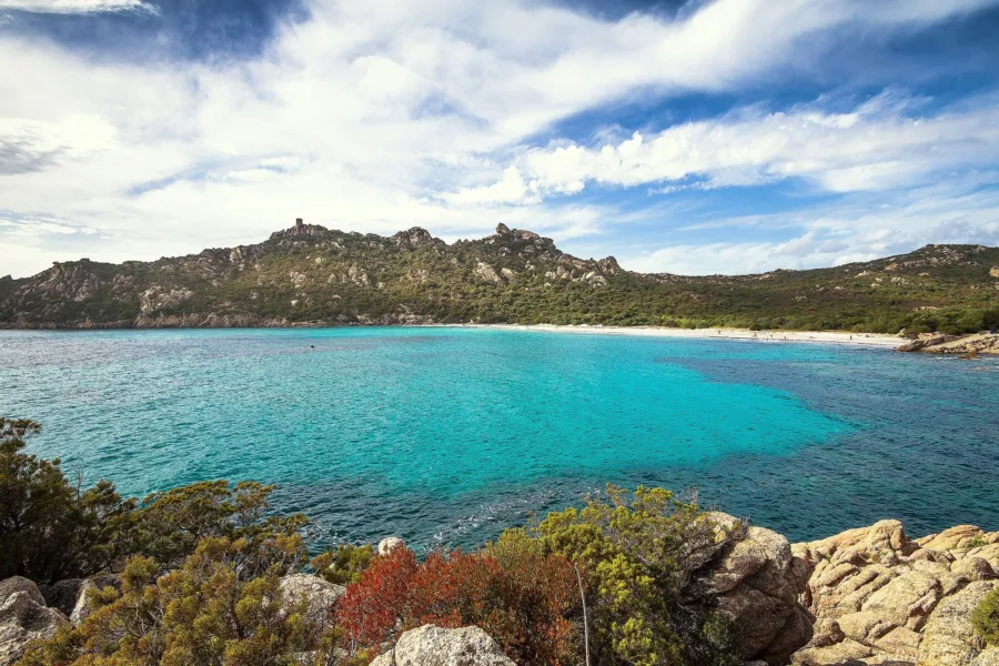 L'anse de Roccapina aux eaux turquoise, avec la tour génoise et le rocher du Lion sur la crête, vus depuis la rive sud du golfe.