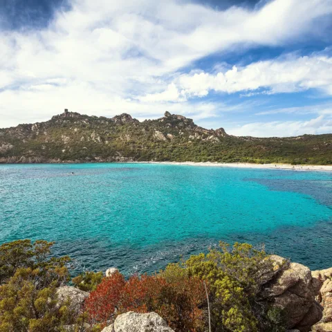 L'anse de Roccapina aux eaux turquoise, avec la tour génoise et le rocher du Lion sur la crête, vus depuis la rive sud du golfe.