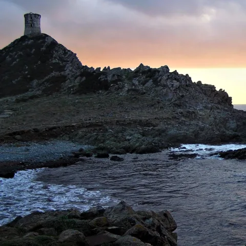 Coucher de soleil à la pointe de la Parata : la tour génoise en silhouette au sommet du promontoire, la mer agitée au premier plan.