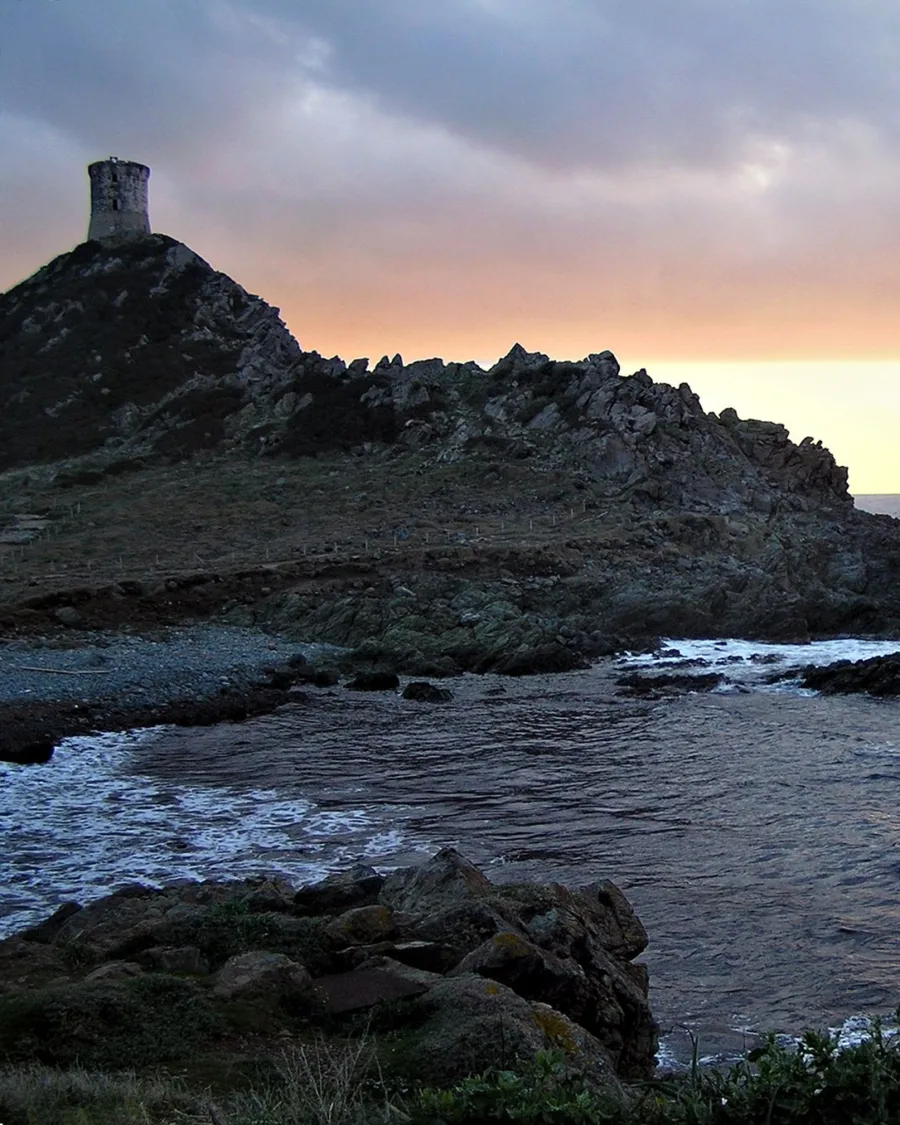 Coucher de soleil à la pointe de la Parata : la tour génoise en silhouette au sommet du promontoire, la mer agitée au premier plan.