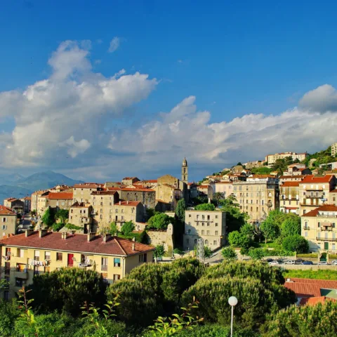 La vieille ville de Sartène, maisons de granit étagées et clocher, sous un ciel de nuages.